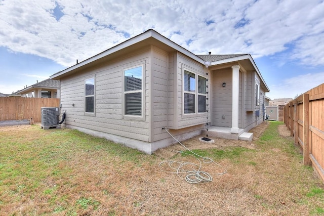 rear view of property featuring a fenced backyard, central AC, and a lawn