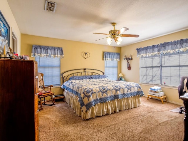 carpeted bedroom featuring ceiling fan, multiple windows, visible vents, and baseboards