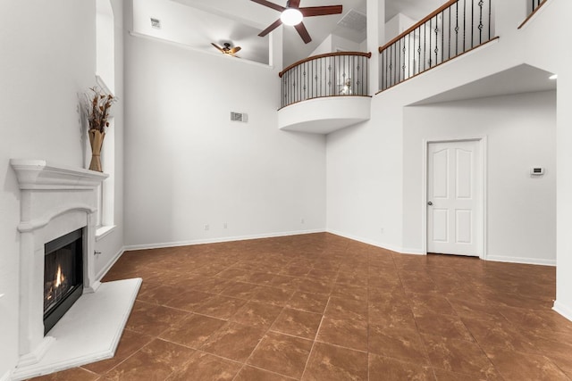 unfurnished living room with a warm lit fireplace, visible vents, baseboards, ceiling fan, and a high ceiling