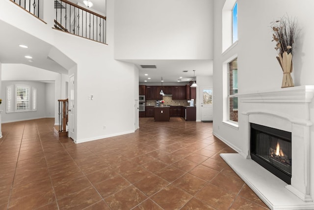 living room featuring visible vents, dark tile patterned flooring, a warm lit fireplace, baseboards, and stairs