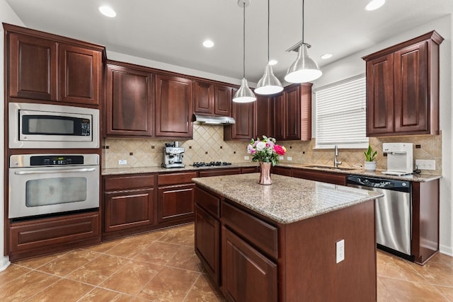 kitchen featuring light stone counters, a center island, decorative light fixtures, appliances with stainless steel finishes, and a sink