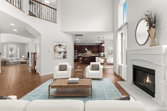 tiled living room featuring recessed lighting, visible vents, a high ceiling, a glass covered fireplace, and baseboards