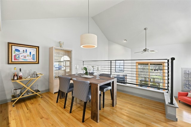 dining space with light wood-style floors, ceiling fan, high vaulted ceiling, and baseboards