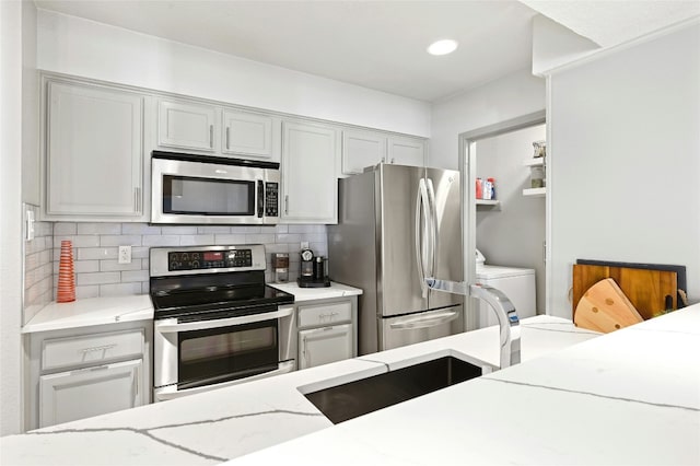 kitchen featuring appliances with stainless steel finishes, washer / clothes dryer, light stone counters, and tasteful backsplash