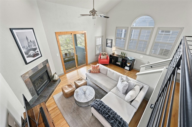 living room featuring a ceiling fan, high vaulted ceiling, wood finished floors, and a tile fireplace