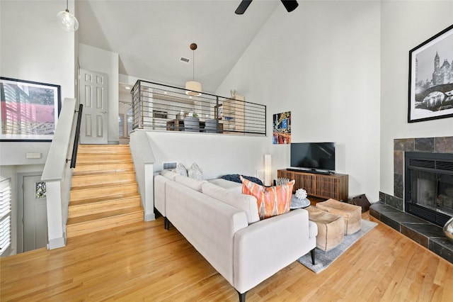 living room featuring visible vents, wood finished floors, stairs, a fireplace, and high vaulted ceiling