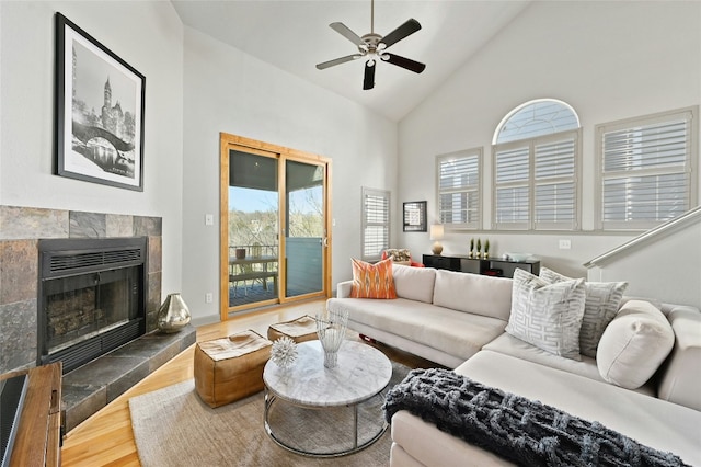 living area with high vaulted ceiling, a fireplace, ceiling fan, and wood finished floors