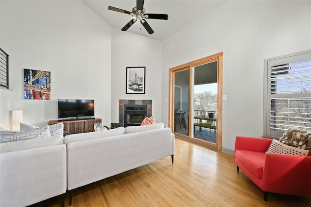 living area with ceiling fan, high vaulted ceiling, a tiled fireplace, and light wood-style flooring