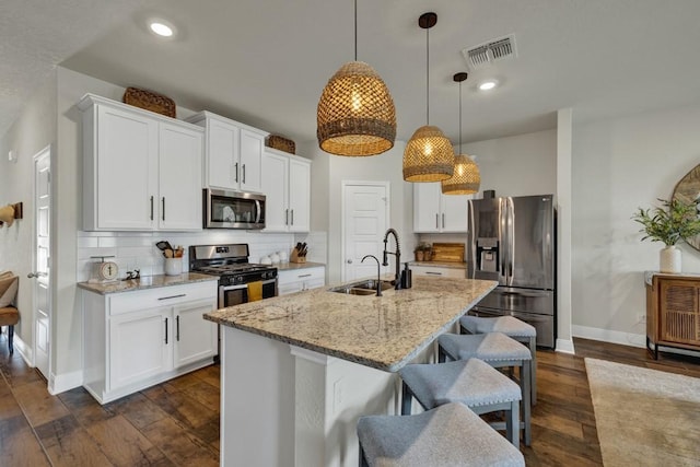 kitchen with stainless steel appliances, tasteful backsplash, visible vents, a sink, and a kitchen bar