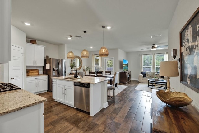 kitchen featuring light stone counters, appliances with stainless steel finishes, dark wood-type flooring, open floor plan, and a sink