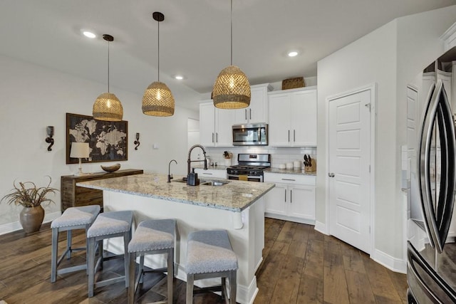 kitchen with decorative backsplash, light stone counters, appliances with stainless steel finishes, dark wood-type flooring, and a sink