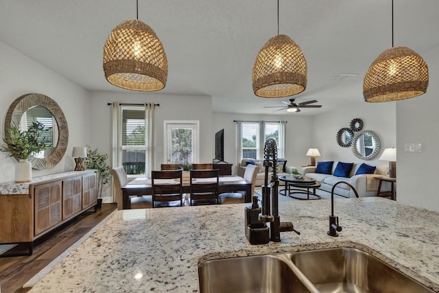 kitchen with hanging light fixtures, a sink, light stone counters, and dark wood-type flooring