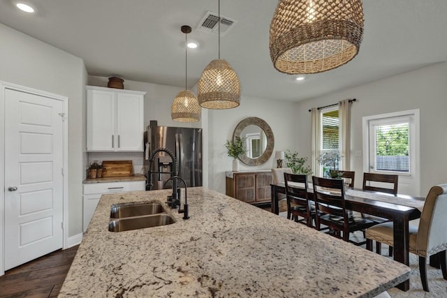 kitchen featuring visible vents, freestanding refrigerator, light stone countertops, white cabinetry, and a sink