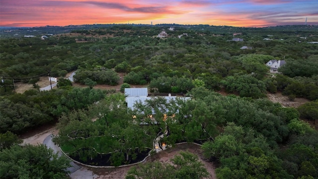 aerial view at dusk featuring a wooded view