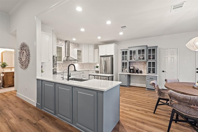 kitchen with wall chimney exhaust hood, freestanding refrigerator, gray cabinets, light wood-type flooring, and a sink