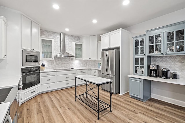 kitchen with white cabinetry, black appliances, light wood-style flooring, and wall chimney exhaust hood