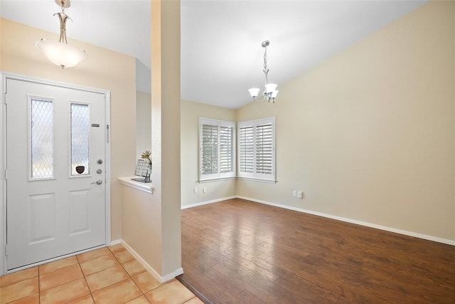 entrance foyer featuring a notable chandelier, vaulted ceiling, light wood-style flooring, and baseboards