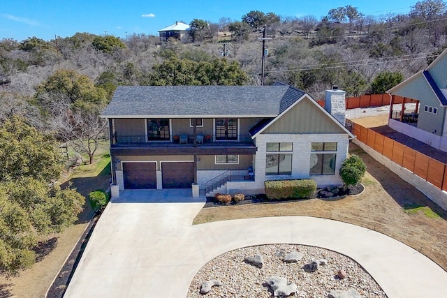 view of front of property with concrete driveway, a balcony, a chimney, an attached garage, and fence