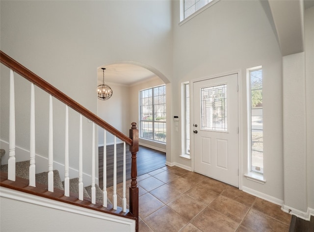 foyer entrance featuring baseboards, stairway, an inviting chandelier, tile patterned flooring, and crown molding