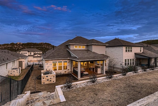 back of property at dusk with stone siding, a fenced backyard, a patio area, and stucco siding