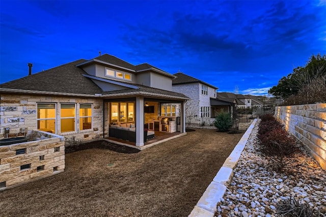 rear view of property with a shingled roof, stone siding, fence, and a patio