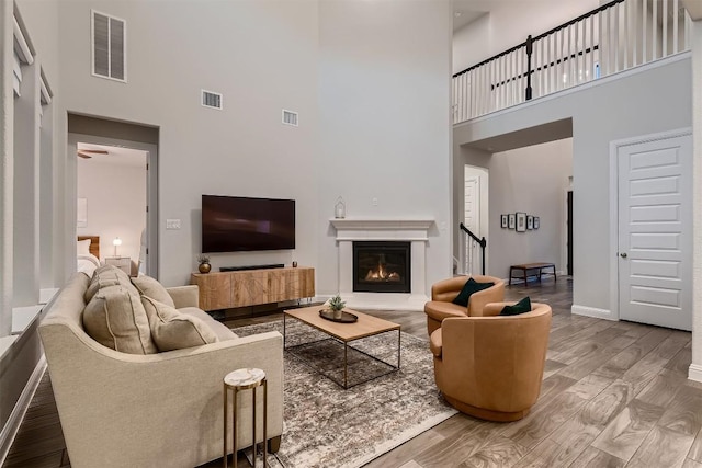 living room featuring a warm lit fireplace, visible vents, and wood finished floors