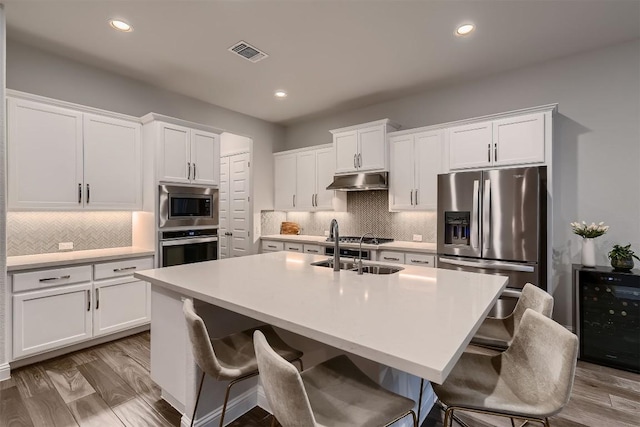 kitchen featuring under cabinet range hood, beverage cooler, stainless steel appliances, visible vents, and white cabinets