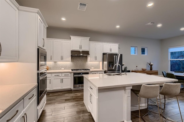 kitchen featuring dark wood-style floors, stainless steel appliances, visible vents, decorative backsplash, and under cabinet range hood