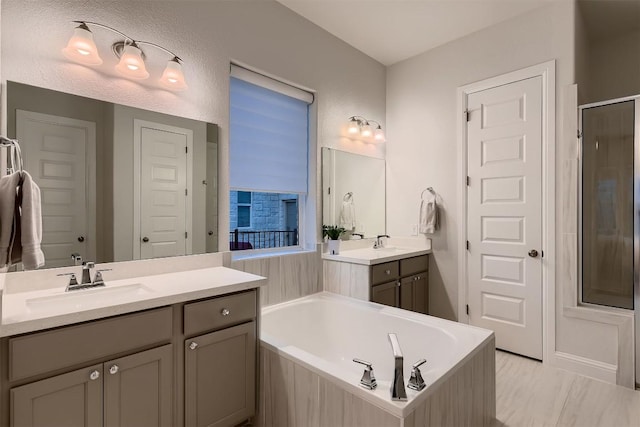 bathroom featuring a bath, an enclosed shower, two vanities, and a sink