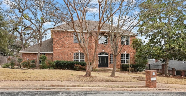 colonial house featuring brick siding, a shingled roof, and fence