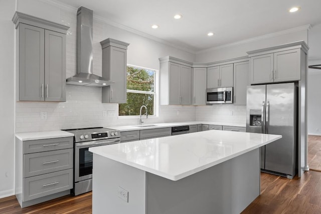 kitchen with gray cabinetry, wall chimney range hood, dark wood finished floors, stainless steel appliances, and a sink