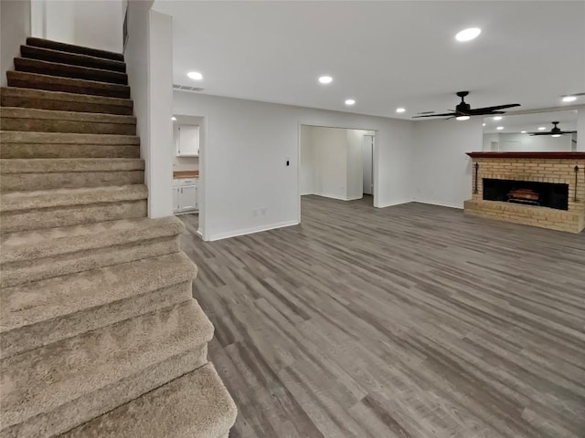 unfurnished living room with ceiling fan, wood finished floors, stairs, a fireplace, and recessed lighting