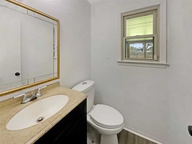 half bath with baseboards, vanity, toilet, and wood finished floors