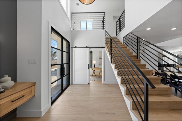 foyer with a barn door, wood finished floors, a towering ceiling, baseboards, and stairs