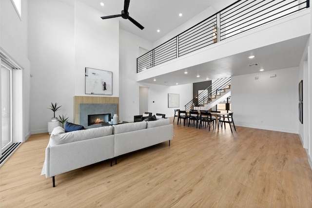 living area with baseboards, ceiling fan, light wood-style flooring, a lit fireplace, and stairs