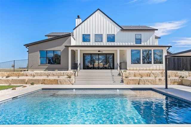 back of property featuring a chimney, fence, an outdoor pool, and board and batten siding