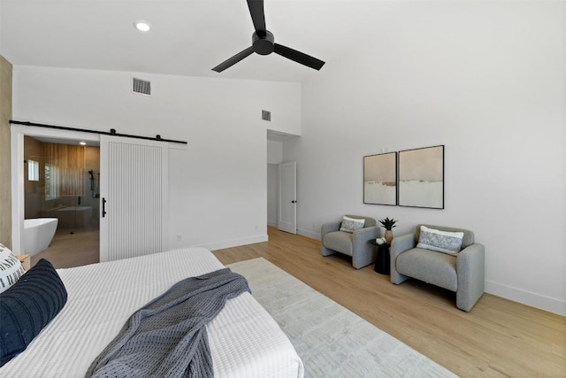 bedroom with a barn door, visible vents, baseboards, light wood-style floors, and high vaulted ceiling