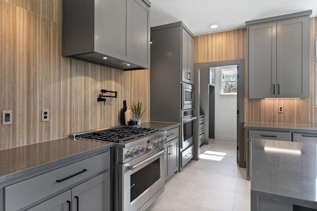 kitchen with stainless steel appliances, wall chimney range hood, light tile patterned flooring, and gray cabinets