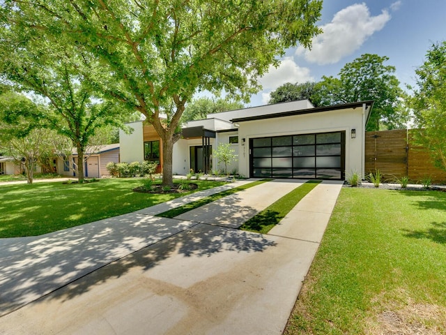 contemporary home featuring concrete driveway, stucco siding, an attached garage, fence, and a front yard