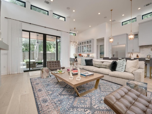 living room with recessed lighting, visible vents, a towering ceiling, and light wood finished floors