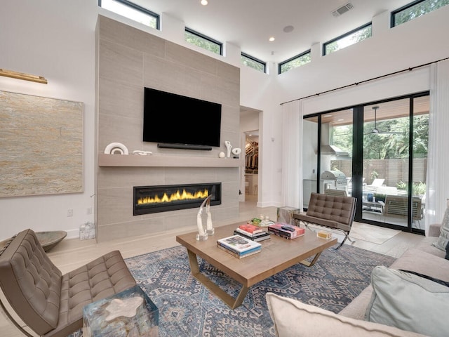 living room with a towering ceiling, a tile fireplace, visible vents, and recessed lighting