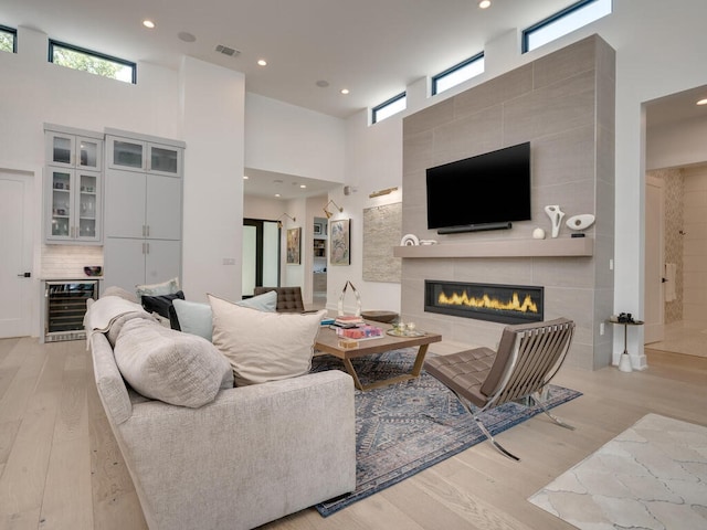 living area with light wood finished floors, visible vents, a tile fireplace, wine cooler, and a high ceiling