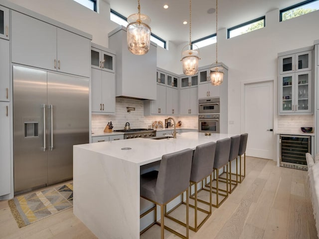 kitchen with beverage cooler, a towering ceiling, appliances with stainless steel finishes, light countertops, and a sink