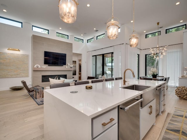 kitchen featuring light wood-type flooring, stainless steel dishwasher, a fireplace, and a kitchen island with sink