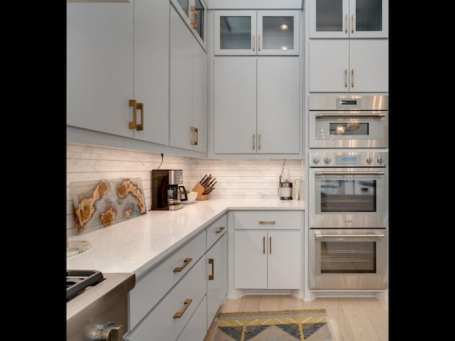 kitchen with tasteful backsplash, glass insert cabinets, white cabinets, and stainless steel double oven