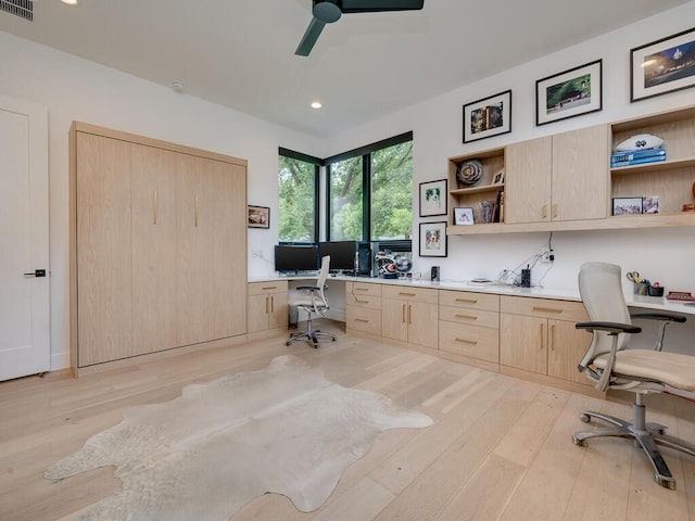 office with light wood-style floors, visible vents, built in desk, and a ceiling fan