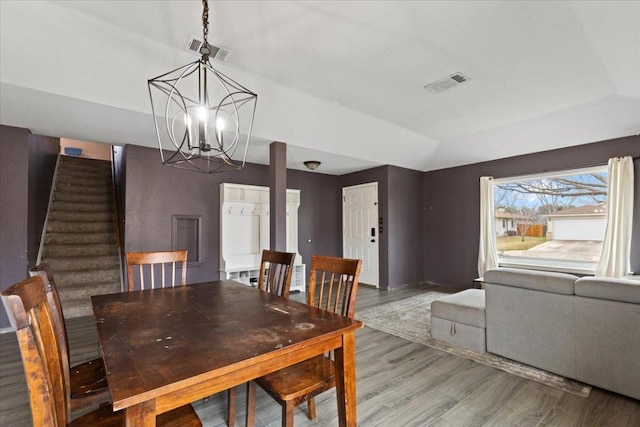 dining space featuring an inviting chandelier, stairs, visible vents, and wood finished floors