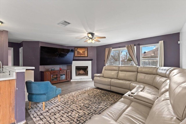 living room with a fireplace, visible vents, dark wood finished floors, and a ceiling fan