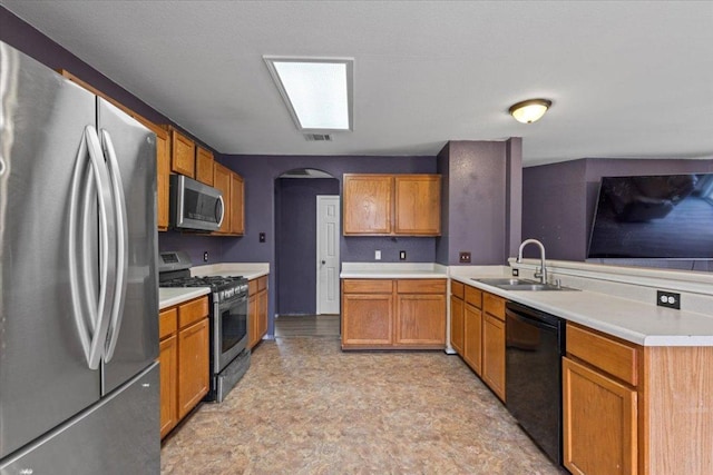 kitchen with arched walkways, a peninsula, a sink, light countertops, and appliances with stainless steel finishes