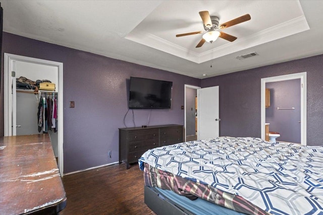 bedroom with wood finished floors, visible vents, a closet, a tray ceiling, and crown molding